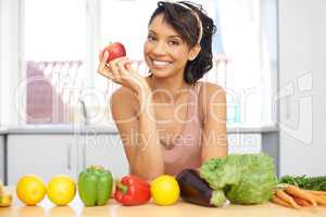 You know what they say about an apple a day.... Portrait of a young woman standing in a kitchen with a line of fresh produce before her.