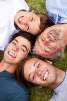 Laughing together through the ages. Father and sons lying down on the grass with their heads beside one another.