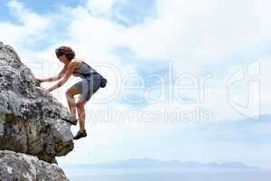 Theres no mountain too high. A woman scaling a rockface on a sunny day.