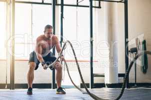 He trains like a superhero. Shot of a muscular young man working out with heavy ropes at the gym.