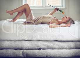 Relaxation and natural aroma. Shot of a beautiful young woman smelling a rose while lying on bed of oversized blankets.