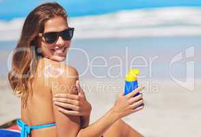 Shield your skin. Shot of a young woman applying suntan lotion at the beach.