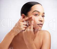 Should I pop it. Studio shot of a beautiful young woman squeezing a pimple on her face against a white background.