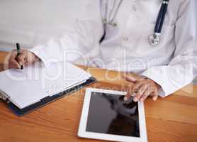 Multi-tasking like a boss. Cropped shot of a doctor using a digital tablet and writing on a sheet of paper.