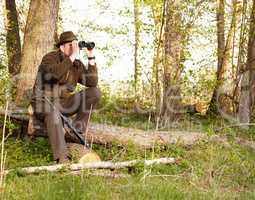 Wildlife hunting requires patience. A game ranger looking through his binoculars while sitting on a log.