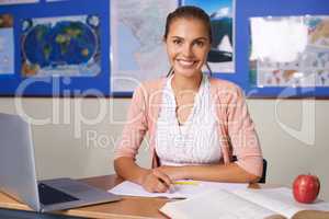 She shapes the leaders of tomorrow. A lovely young teacher sitting at her desk and smiling at the camera.