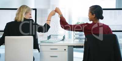 Today we outdid ourselves. Rearview shot of two young businesswomen pounding their fists in succession while being seated at their desk in the office.