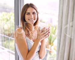 Starting the day with sunshine and coffee. Shot of an attractive young woman standing by the sliding door while enjoying a cup of coffee.
