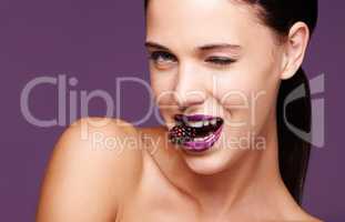 Berry berry nice. A studio portrait of a beautiful young woman wearing purple lipstick and biting into a berry.