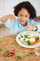 Playing with your food. A cute young boy throwing peas from his plate all over the table.