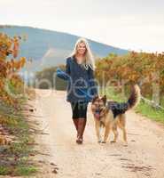 Getting some fresh air. Portrait of a pretty young woman walking her Alsatian in a vineyard.