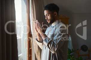 Prayer is the surrender of all fears. Shot of a young muslim man praying in the lounge at home.