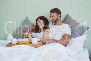 Where should we start. Shot of a cheerful young couple sitting in bed while enjoying breakfast together during morning hours.