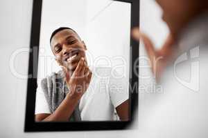 No irritation, no redness. Cropped shot of a young man touching his face while looking into the bathroom mirror.