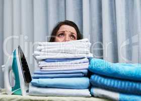 Too much to do, too little time. Shot of an anxious looking young woman behind a pile of laundry on an ironing board.
