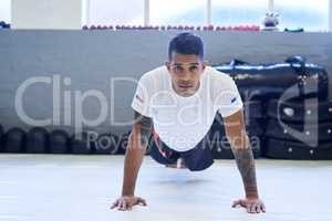 Working on my upper body strength. Portrait of a young man doing pushups in the gym.