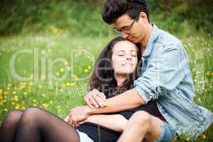 Sharing a sweet bond. Young couple sitting together affectionately in a springtime field.