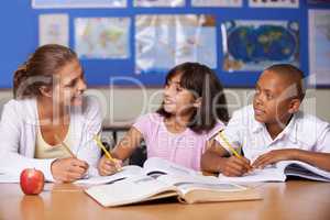 Giving some positive reinforcement. A young teacher having a discussion with her two ethnic pupils while they page through a textbook.