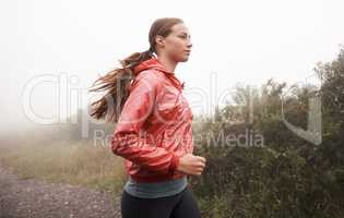 The only way to run. Shot of a young female jogger in a misty country road in the morning.