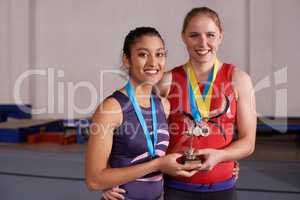 Talent wins games, teamwork wins championships. Portrait of two young medalists holding a trophy together.