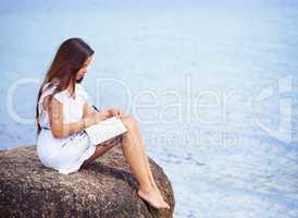 Profound insights surrounded by tranquil nature. Full length shot of a gorgeous tattooed young woman sitting on a rock writing in a diary.