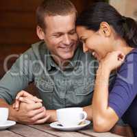 They share the same silly humour. A young multi-racial couple laughing together while drinking coffee at a cafe.