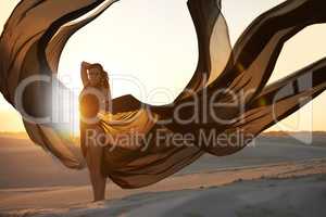 Freedom and isolation for a goddess. Shot of a beautiful young woman in swimwear holding flowing dark material at sunset.