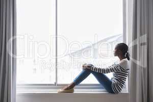 Her favourite spot to daydream. A beautiful young woman lost in thought while sitting on a window sill.