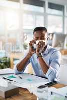 Hes booking an appointment with the doctor right away. Shot of a sickly young businessman taking a phone call while covering his nose with a tissue in his office.