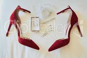The essential details for a bride. Closeup of various amounts of fine elegant jewelry and a pair of red high heels resting against a white sheet.