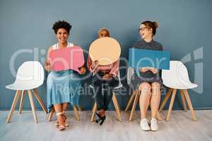 I think I shouldnt have said that. Studio shot of a group of attractive young businesswomen holding speech bubbles while sitting in a row against a grey background.