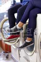 Waiting for their washing. Cropped image of a couples legs and feet as they sit on a washing machine at the laundry.