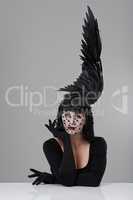 It takes all kinds. Shot of a young woman in a wing-shaped headpiece sitting in a studio.