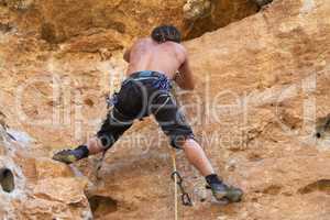 Climbing the rugged rockface. Rearview of rugged bare chested rock climber climbing a rockface.
