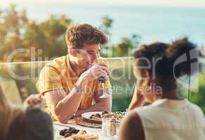 If only these type of moments can last forever. Shot of a handsome young man enjoying a glass of wine while sitting around a table with friends outdoors.