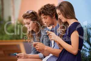 None of those awkward silent moments here.... Three young adults using their cellphones while sitting outdoors.