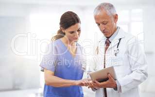 Comparing medical records. Shot of two medical professionals looking at a digital tablet.