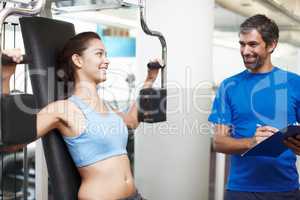 Am I doing this correctly. Cropped shot of an attractive young woman using an exercise machine while her personal trainer looks on.