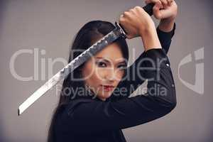 Ready for your challenge. Studio portrait of a beautiful young woman in a martial arts outfit wielding a samurai sword.