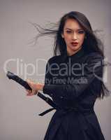 Unsheathing her blade. Studio portrait of a beautiful young woman in a martial arts outfit wielding a samurai sword.
