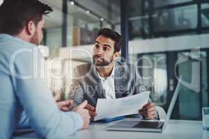 Statistical analysis that tell a story of success. Shot of two young businessmen using a laptop while going through paperwork together in a modern office.