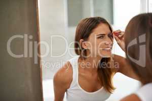 Being beautiful can be a bit painful someitmes. Shot of a young woman painfully tweezing her eyebrows in a bathroom mirror.