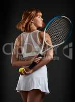 Tennis is more than just a sport. Cropped shot of a woman posing with a tennis racket and ball against a dark background.