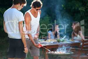 Grilling the meat to perfection. Young guys barbequing meat on the grill outdoors - Lifestyle.
