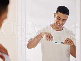 Dental hygiene is a must. Shot of a handsome young man standing alone in his bathroom and brushing his teeth in the morning.