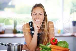Skip the diet, just eat healthy. Portrait of a young woman leaning on her kitchen counter with a pot and vegetables next to her.