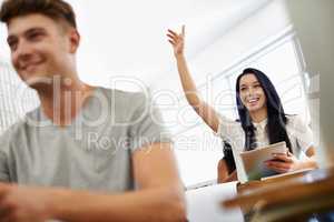 Working her way towards a distinction. A young woman raising her hand as she sits in a varsity class surrounded by her peers.