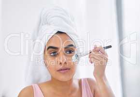 Why spend so much money when you can DIY. Shot of a woman using a paintbrush to apply a product to her face.