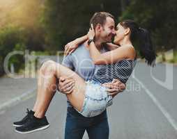 Youre my knight in shining armor. Shot of a young man romantically carrying his girlfriend down a road outdoors.