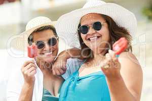 The perfect summer cool down. Shot of two mature friends standing together and enjoying ice cream while bonding on the beach during the day.